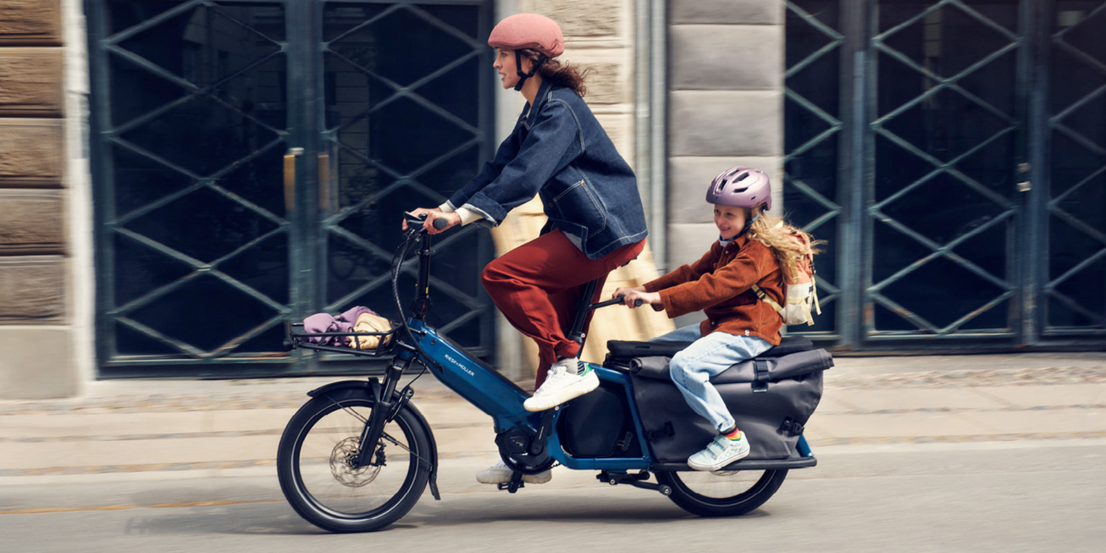 A woman riding a Riese and Muller Multitinker cargo bike with a child on the back